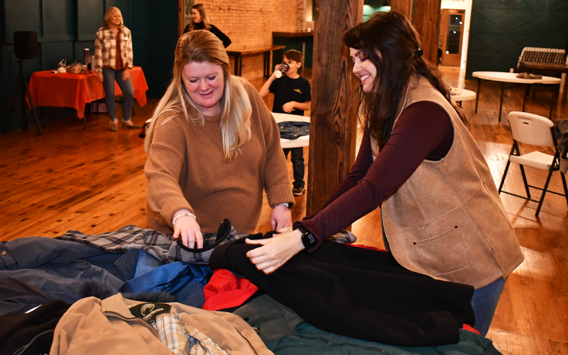Kiara Mealor of Jack Bradley Agency and Rebecca Glaze with the Family Resource Center organize coats donated as part of a coat and sock drive at Common Ground in Cornelia on Tuesday night. MATTHEW OSBORNE/Staff