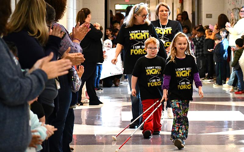 Students cheer on Monroe Bogue (left) and Phoebe Groves (right) as they strut down the Fairview Elementary School hallways with their white canes. Vision teacher Robin Skelton (left) and vision paraprofessional Sherry Crain (right) follow the two students. JULIANNE AKERS/Staff