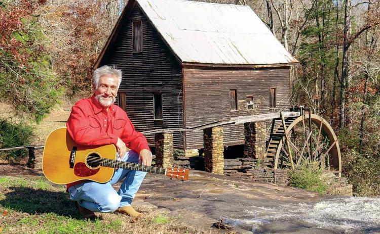 Musician Danny Thomas poses with his guitar in front of Ragsdale Grist Mill in Homer (Banks County).