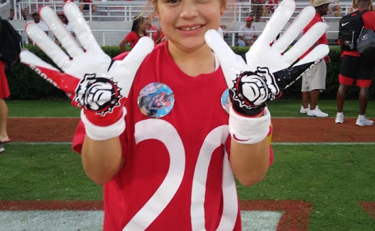 Michaela Krippner, 11, of Mt. Airy, holds up a pair of game-worn gloves gifted to her by University of Georgia safety J.R. Reed.
