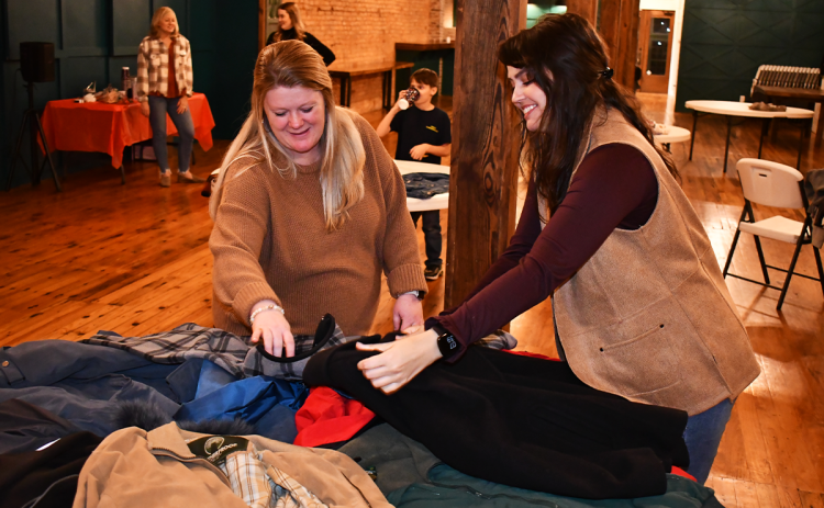 Kiara Mealor of Jack Bradley Agency and Rebecca Glaze with the Family Resource Center organize coats donated as part of a coat and sock drive at Common Ground in Cornelia on Tuesday night. MATTHEW OSBORNE/Staff