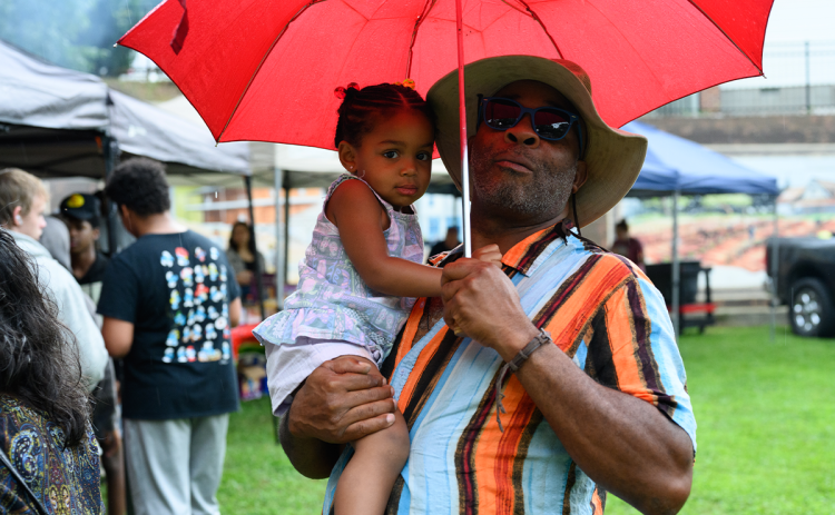 Willie Savage (right) and Callie Kimbroke (left) stand under an umbrella while waiting for the free hotdogs and hamburgers provided by the City of Baldwin. ZACH TAYLOR/Special
