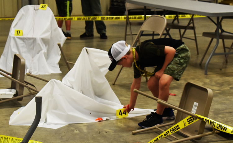 Conner Arrowood, one of the students taking part in the Crime Scene Camp, places an evidence marker on something he thinks will help them solve the crime. EMMA MARTI/Staff