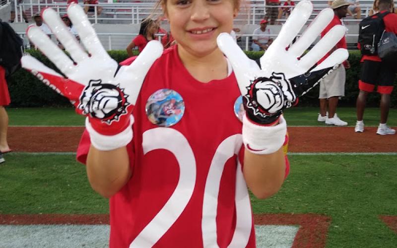 Michaela Krippner, 11, of Mt. Airy, holds up a pair of game-worn gloves gifted to her by University of Georgia safety J.R. Reed.