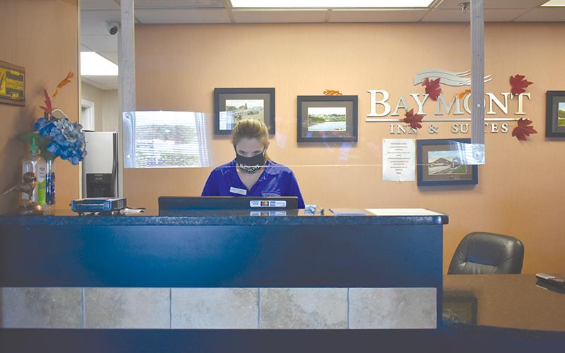 A sheet of plexiglass hangs from the ceiling between guests and Heather Boyd, who works at the front desk at the Cornelia Baymont Inn &amp; Suites, under a new set of protocols to prevent the spread of COVID-19.