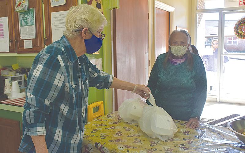 Geri Johnson hands a meal packaged in to-go boxes to Mary Burns at the Clarkesville Soup Kitchen on Monday morning.