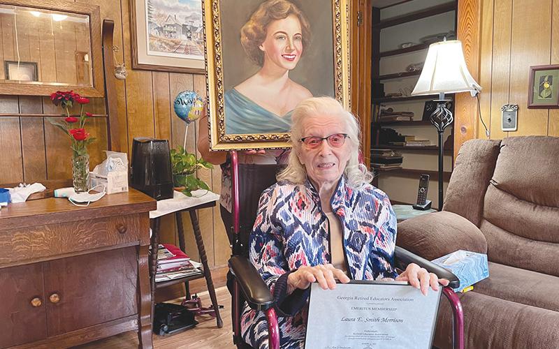 Laura Morrison holds her certificate from the Georgia Retired Educators Association, while her caretaker shows off a portrait of Morrison in her 20’s behind her. BRIAN WELLMEIER/Special