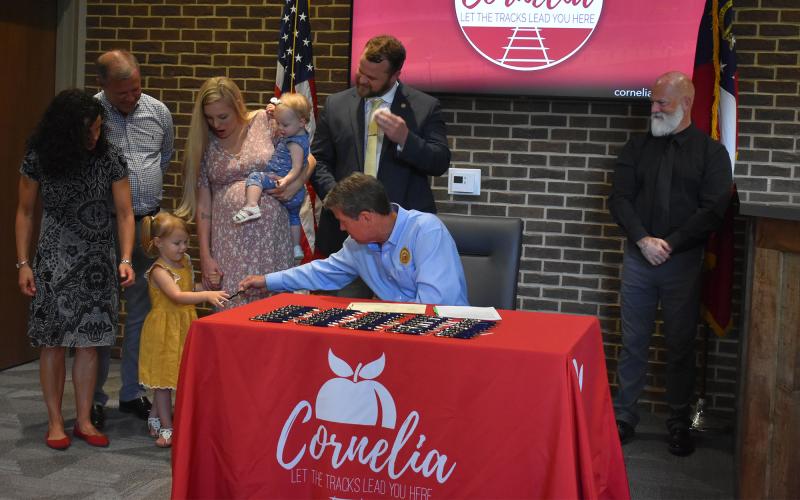 Gov. Brian Kemp hands a pen to Hallie Hatchett, oldest daughter of Sen. Bo Hatchett and his wife Ashley. Also shown are Missy Hatchett, Dr. Bo Hatchett, little Hazel and sign language expert David Cowan (right). CHAMIAN CRUZ/Staff