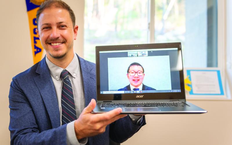 TFS teacher Adam Grieving holds up a computer with a smiling Pengyue "Peter" Wang.