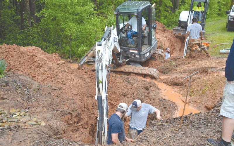 Workers from Demorest’s water department look to repair the pipe damaged Tuesday morning by a freak lightning strike that melted at least one section of a water pipe (inset) and left a trench through the woods. MATTHEW OSBORNE/Staff
