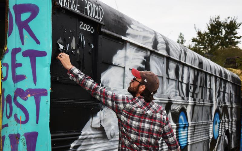 Artist Nick Morris peels some chipped paint from one of the buses. MATTHEW OSBORNE/Staff