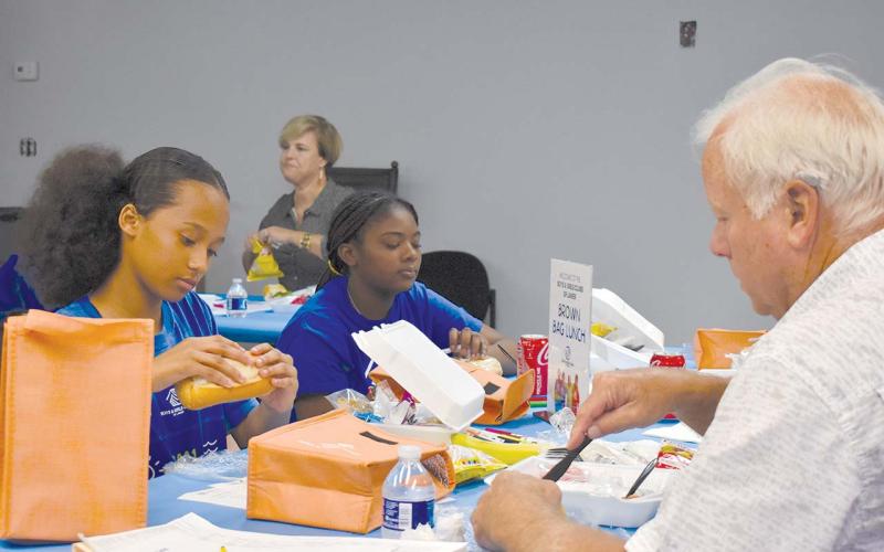 Rising 7th grader London Garcia (left) and rising 8th grader Raigen Mathis (right) eat lunch across from Wade Rhodes, Board Chair at the Tim Lee Boys &amp; Girls Club. EMMA MARTI/Staff