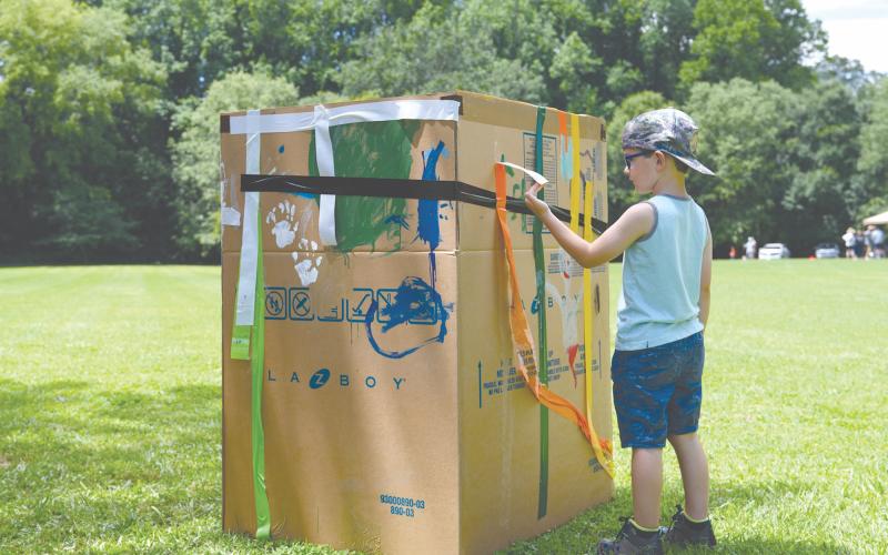 Mason Reeder places the final touches of orange duct tape on the cardboard boat he and other children painted in Pitts Park on Saturday. The cardboard boat race was postponed due to unsafe river conditions after the rain throughout the week. ZACH TAYLOR/Special