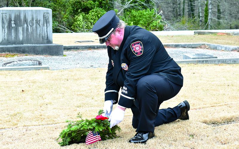 Demorest Interim Fire Chief Jerry Palmer kneels as he places a wreath on his grandfather’s grave at the first Wreaths Across America event at Demorest City Cemetery on Saturday morning. MATTHEW OSBORNE/Staff