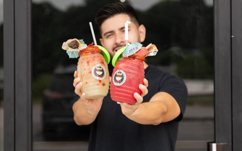 Luis Covarrubias of Raspas El Tigre in Cornelia holds a watermelon agua fresca and cucumber-lime agua fresca topped with ice cream and candy. The sweet treats can help folks stay cool in the heat of the summer. ZACH TAYLOR/Special