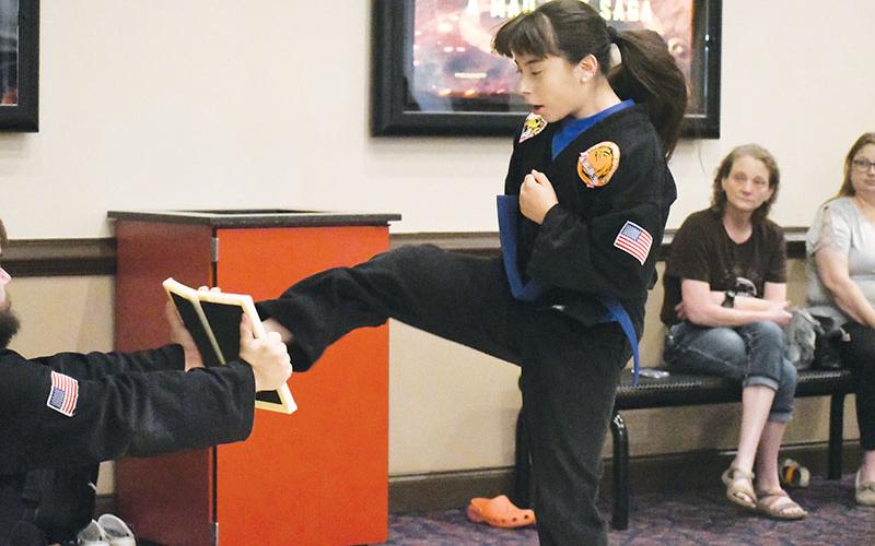 Blue belt Abril Rodriguez mid-jump before kicking in half a board held by third degree black belt Billy McCoy in the lobby of Habersham Hills Cinema on Tuesday morning.
