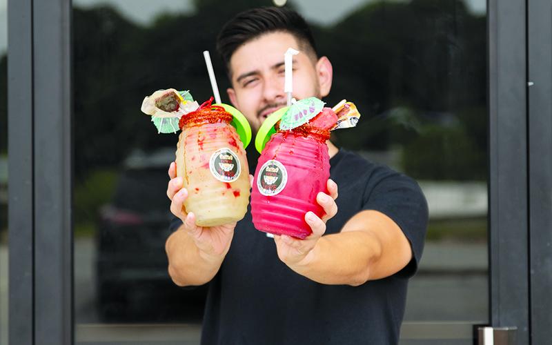 Luis Covarrubias of Raspas El Tigre in Cornelia holds a watermelon agua fresca and cucumber-lime agua fresca topped with ice cream and candy. The sweet treats can help folks stay cool in the heat of the summer. ZACH TAYLOR/Special