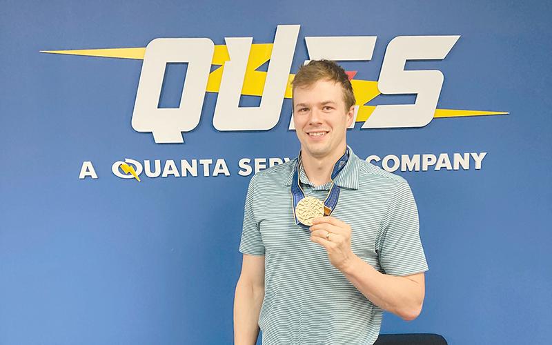 Nic Fink holds up his 2023 World Championship gold medal at Quanta’s Atlanta office. He’ll return from France with an Olympic medal to add to his collection.