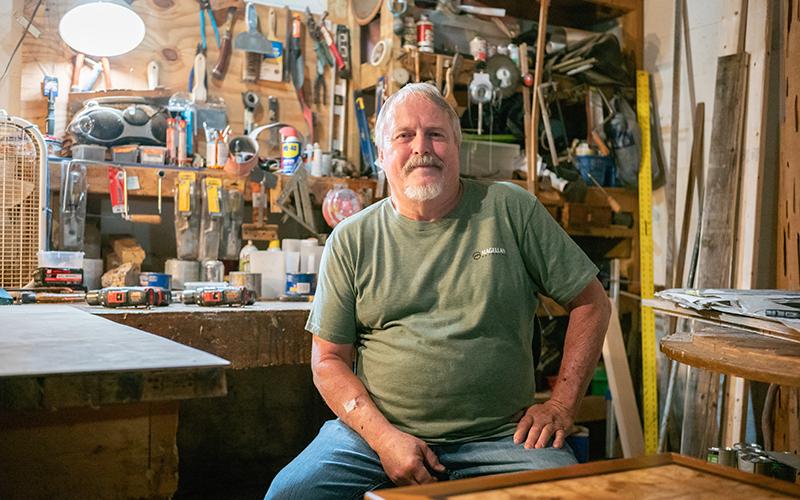Local woodworker Dennis Banks sits for a portrait in his basement’s dimly lit shop bench area. He considers his shop to be ‘messy’ but highly productive. Every month, Banks produces around ten pieces of original master woodworking art in the form of tables. ZACH TAYLOR /Staff