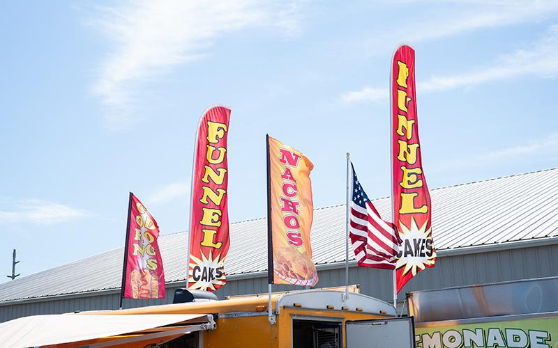 Flags advertising funnel cakes, nachos and corn dogs wave in the wind. This year’s fair will have no shortage of food ranging from lemonade to Korean BBQ. ZACH TAYLOR/Staff