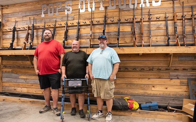 ZACH TAYLOR/Staff Whit Aikens, Dale Hope and Greg Hope stand before the wall of firearms for sale in Pop’s Outdoors. The trio have worked together for over a decade in the outdoors and hunting industry. ZACH TAYLOR/Staff