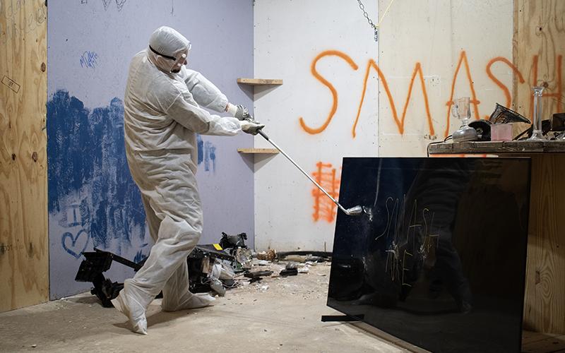 Christopher Davidson breaks an old television with a golf club in one of Smash It’s several “smash rooms.” JULIANNE AKERS/Staff