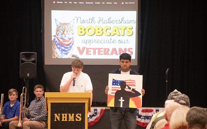 NHMS student Rugar Bramlett reads a poem honoring veterans while Sergio Vazquez holds up artwork. JULIANNE AKERS/Staff