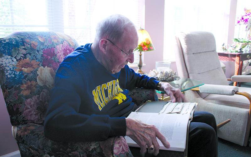Ken Schubring flips through photographs documenting the bombing at Pearl Harbor, as well as his own account of his service in Hawaii and beyond. HANNAH CAUDELL/Staff