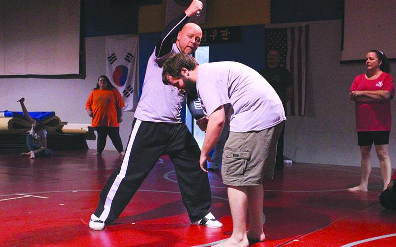Bobby Popham (left) demonstrates how to use an attacker’s momentum against him with William McCoy (right) supporting. HANNAH CAUDELL/Staff