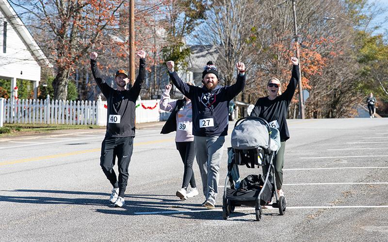 Trent McClure, Abigail Rider, Peyton Rider and Abby McClure cross the finish line, arms raised, with Zoe McClure in the stroller. ZACH TAYLOR/Staff