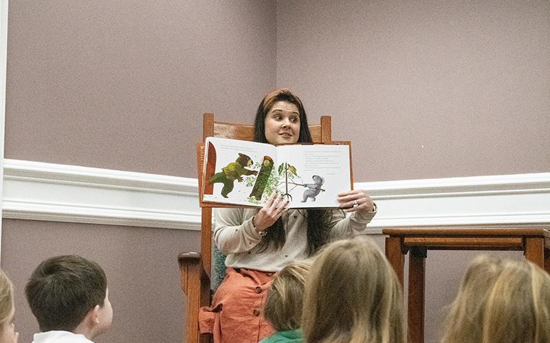 Amanda Almazan, the Clarkesville Library’s youth services coordinator, takes a seat in the rocking chair amongst the children sitting at her feet to read this year’s pick for the featured title, Wombat Said Come In by Carmen Agra Deedy. HANNAH CAUDELL/Staff