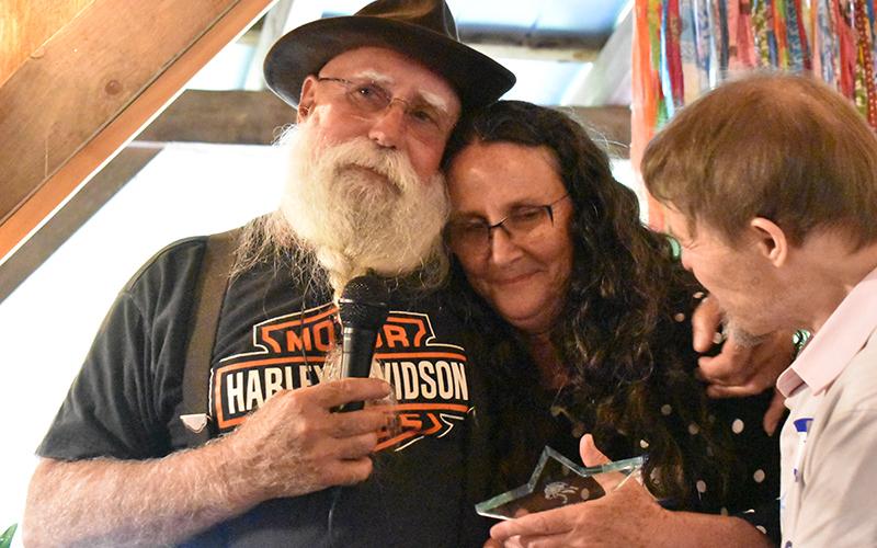 Victor Eller (left) hugs Denise (right) as she holds a recognition award for her many years of service as Avita. Denise retires from a career spanning almost four decades as a leader in the Avita community. HANNAH CAUDELL/Staff