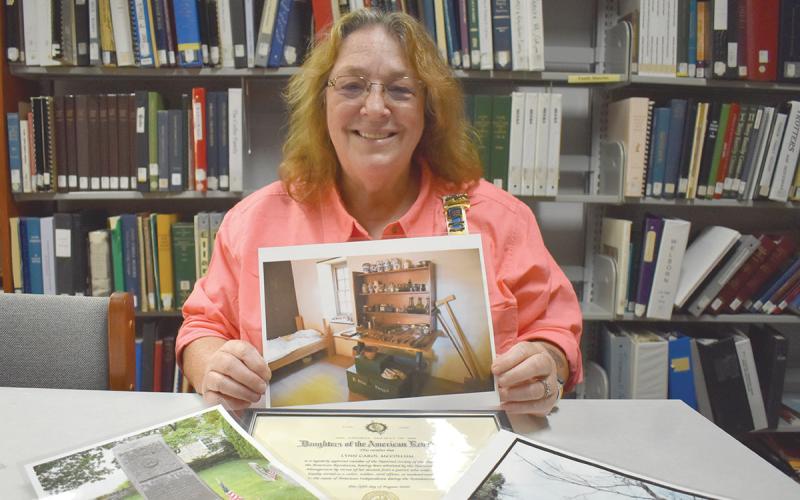 Lynn McCollum holds a photo of the display of Dr. Bodo Otto’s tools at the Old Barracks Museum in Trenton, N.J. Her certificate of membership for the National Daughters of the American Revolution is surrounded by photos and documents sharing some of the history of her Revolutionary War ancestors. (Samantha Sinclair/Staff)