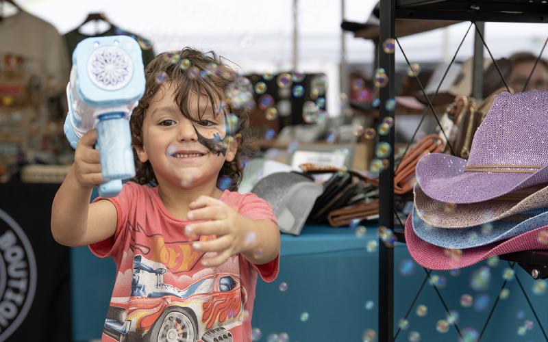 Wyatt Swain blows bubbles at the camera while waiting at a booth at the Big Red Apple Festival in Cornelia. (Zach Taylor/Staff)
