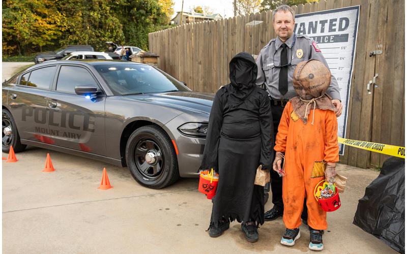 Mt. Airy Police Chief Jamie Bowden stands with Michael Kiser and Jackson Kilmete in front of the police car and a wanted poster at the Mt. Airy Trunk or Treat Saturday. The Bowdens set up a whole scene promoting the police department, which was flush with fake cash, fidget poppers and candy. (Zach Taylor/Staff)