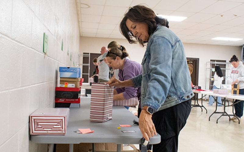 Volunteer Karen Tench grabs another piece of tape to secure the wrapping paper around a new pair of shoes. (Hannah Caudell/Staff)