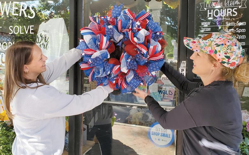 Amber Gilbert and Owner Dale Jones of All in Bloom hang one of the patriotic wreaths they made for Clarkesville’s Red, White and Blue Wreath Display. (Samantha Sinclair/Staff)