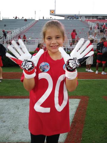 Michaela Krippner, 11, of Mt. Airy, holds up a pair of game-worn gloves gifted to her by University of Georgia safety J.R. Reed.