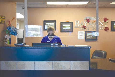 A sheet of plexiglass hangs from the ceiling between guests and Heather Boyd, who works at the front desk at the Cornelia Baymont Inn & Suites, under a new set of protocols to prevent the spread of COVID-19. 