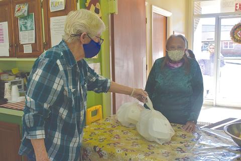 Geri Johnson hands a meal packaged in to-go boxes to Mary Burns at the Clarkesville Soup Kitchen on Monday morning.