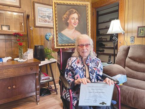 Laura Morrison holds her certificate from the Georgia Retired Educators Association, while her caretaker shows off a portrait of Morrison in her 20’s behind her. BRIAN WELLMEIER/Special