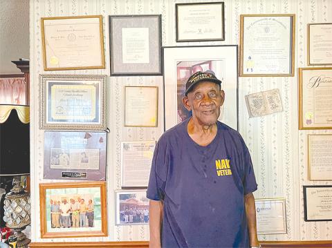 Mordecai Wilson stands by the many awards that adorn the wall of his Lula home.