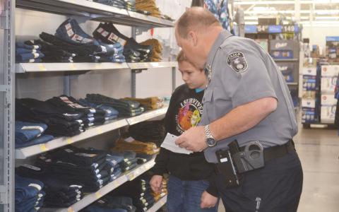 Baldwin Police Chief Jeff Branyon scans the shelves with Jacob, a Baldwin Elementary student, in search of the right pair of jeans at the shopping event Wednesday. BRIAN WELLMEIER/Staff
