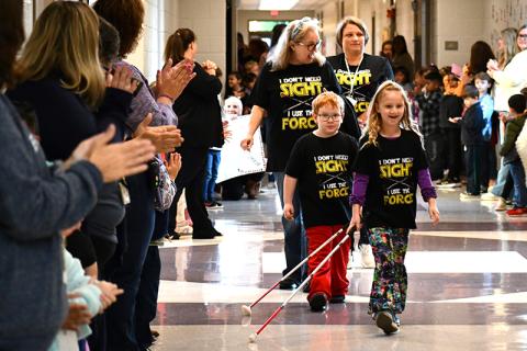 Students cheer on Monroe Bogue (left) and Phoebe Groves (right) as they strut down the Fairview Elementary School hallways with their white canes. Vision teacher Robin Skelton (left) and vision paraprofessional Sherry Crain (right) follow the two students. JULIANNE AKERS/Staff