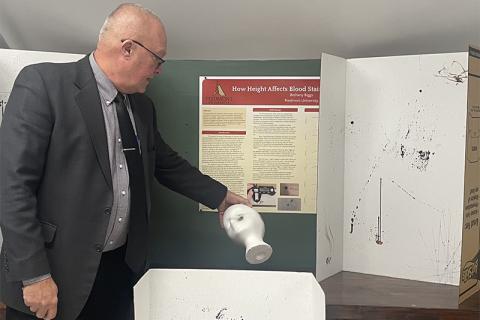 Piedmont University Vice President of Academic Affairs Bruce Willis holds an example of a gunshot wound to the head next to students’ assignments on trajectory of blood stains. JULIANNE AKERS/Staff