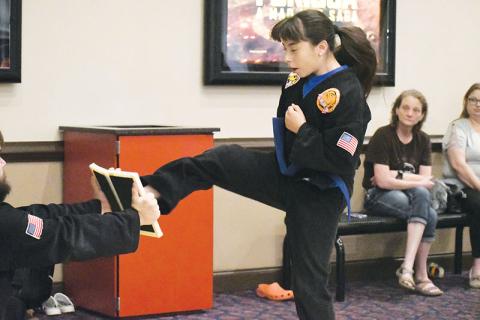 Blue belt Abril Rodriguez mid-jump before kicking in half a board held by third degree black belt Billy McCoy in the lobby of Habersham Hills Cinema on Tuesday morning.