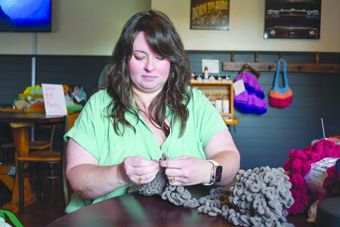 Shannon Trotter knits a scarf using just her hands as she sits in BSG Coffee and Cafe. Some of her other creations hang on the wall behind her. JULIANNE AKERS/Staff 