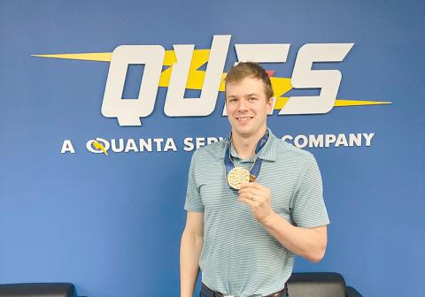 Nic Fink holds up his 2023 World Championship gold medal at Quanta’s Atlanta office. He’ll return from France with an Olympic medal to add to his collection.
