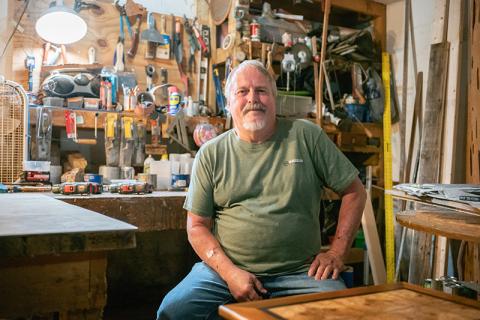 Local woodworker Dennis Banks sits for a portrait in his basement’s dimly lit shop bench area. He considers his shop to be ‘messy’ but highly productive. Every month, Banks produces around ten pieces of original master woodworking art in the form of tables. ZACH TAYLOR /Staff