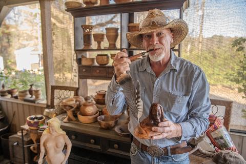 Kenneth Adams stands next to a collection of completed pieces, holding a carved Native American man with feathers and a handmade pipe from his collection of past works. He carves and turns many pieces of wooden art each month, ranging from projects that have lasted years to spontaneous projects that come to his mind on three-day weekends. ZACH TAYLOR/Staff